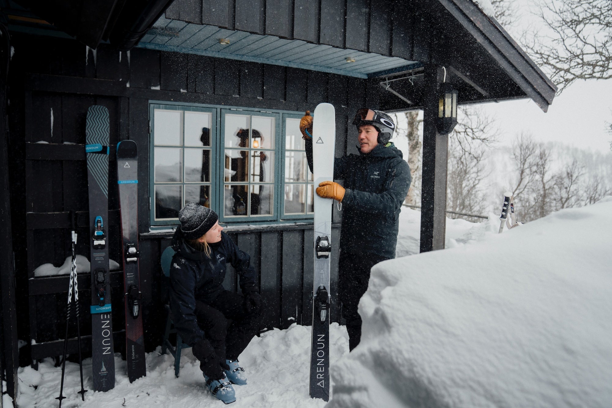 Man and woman standing outside of a ski lodge discussing the different Renoun ski models available to them.