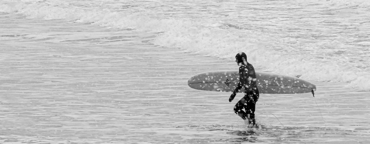 Sophie wearing her wetsuit and carrying her surfboard up the beach
