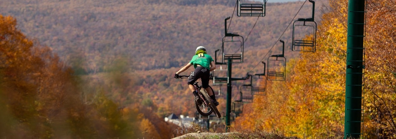 Man mountain biking and doing a jump under a ski lift at Burke Resort and Kingdom Trails Network in Vermont