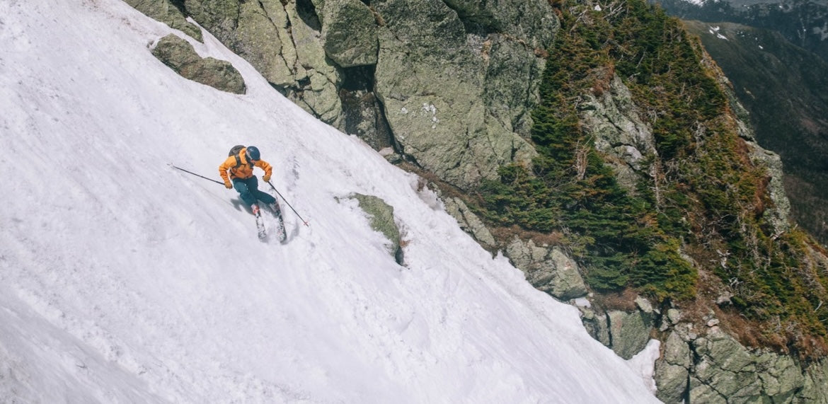 Renoun athlete Matt Testa going backcountry skiing in the summer time on a beautiful day next to a tree and rocks