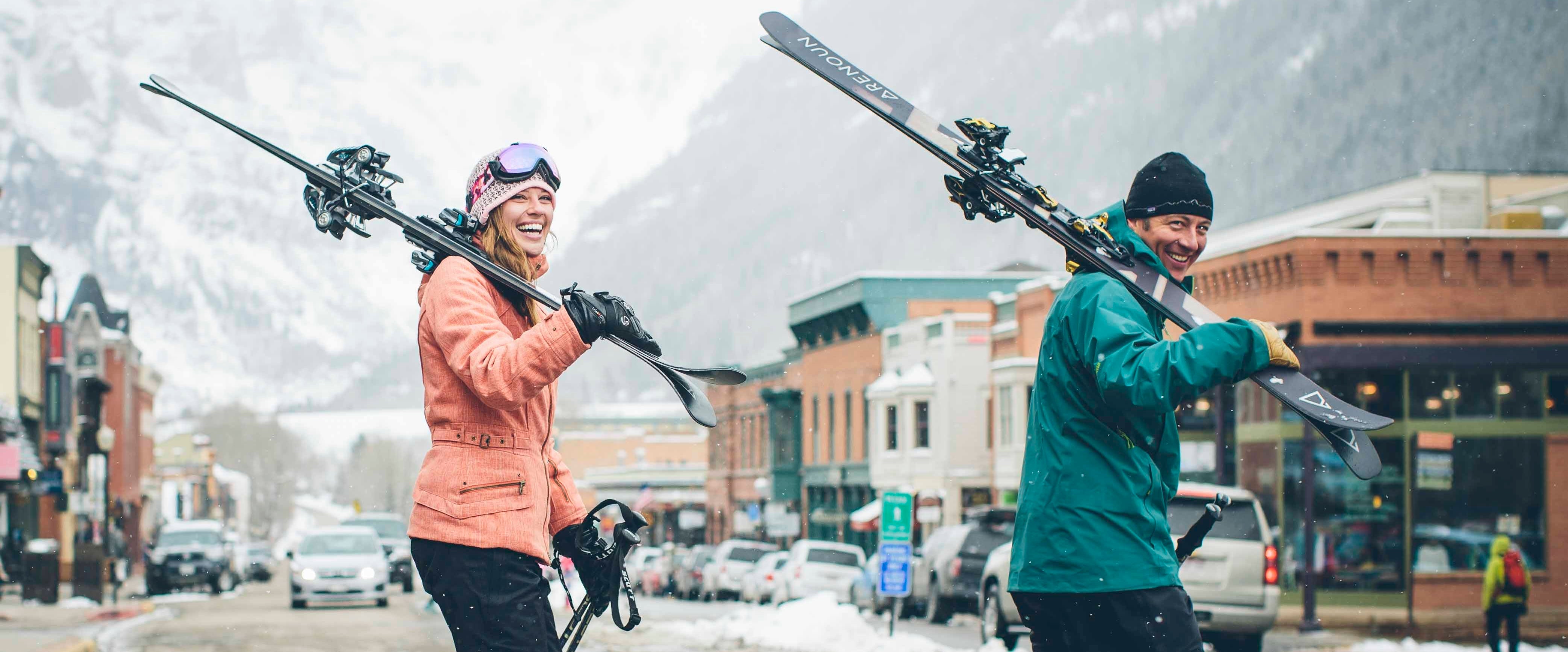 Skiing couple walking across the street in Telluride CO holding Renoun skis