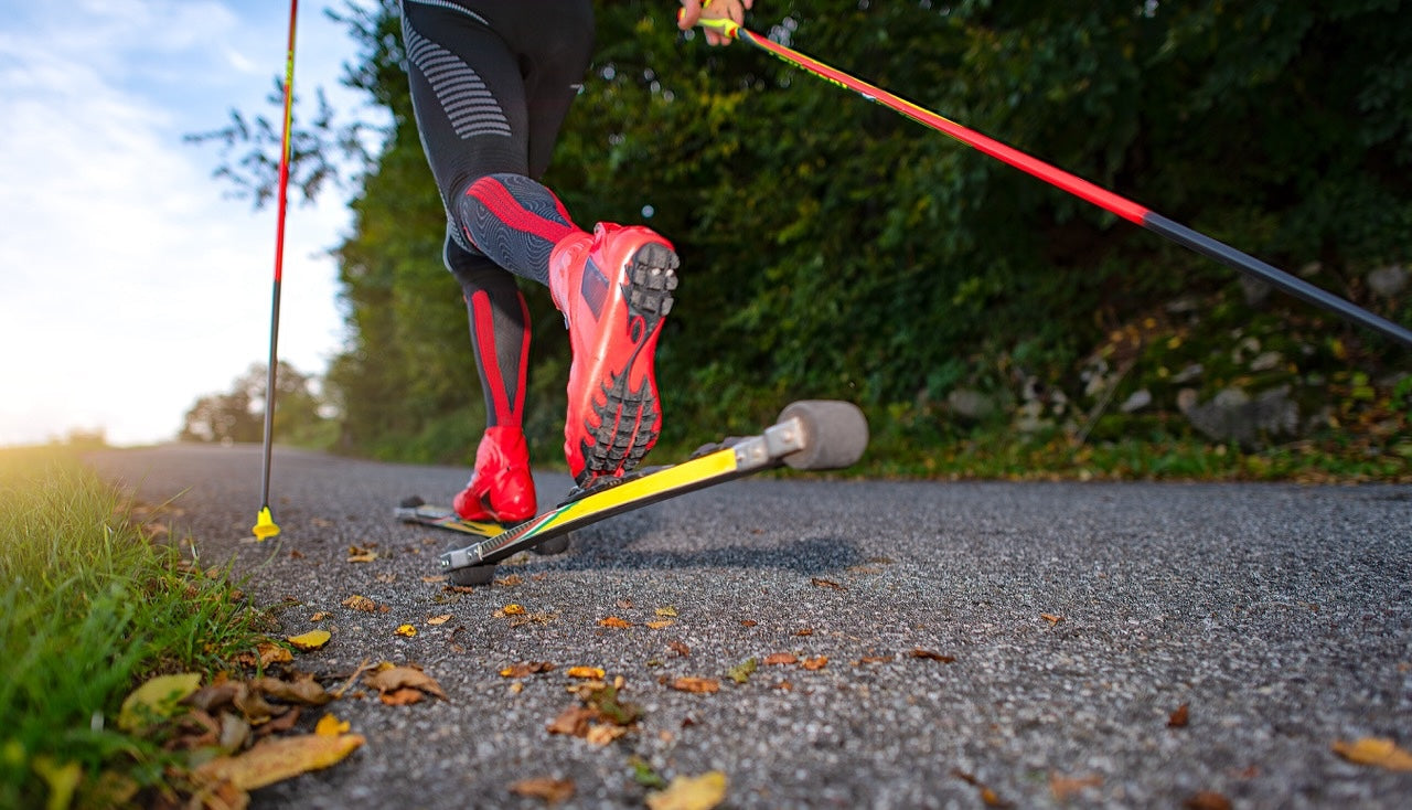 Person using roller skis on a leaf-blown path. Yellow roller skis with red boots